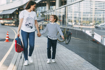 The mother carries a backpack in one hand, and holds her son by the other hand. 