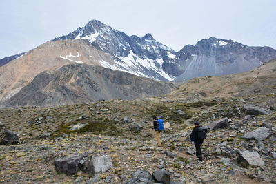 Rear view of people walking on snowcapped mountain against sky