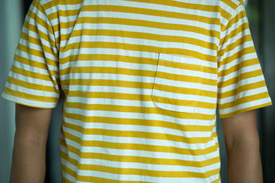 Midsection of man wearing yellow ad white striped t-shirt at home