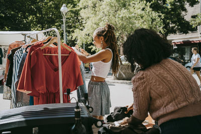 Side view of female customer hanging dress in rack at while shopping at flea market