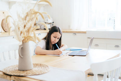 Schoolgirl girl makes homework at the table in front of a laptop. distance learning. 