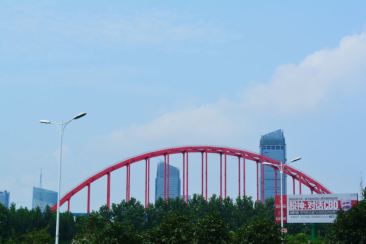 low angle view, built structure, architecture, sky, tree, connection, street light, building exterior, bridge - man made structure, day, outdoors, clear sky, blue, no people, flag, city, american flag, cloud, communication, engineering