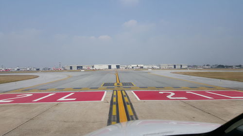 Road by airport runway against sky