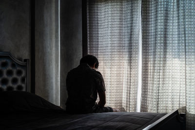 Rear view of man sitting on bed