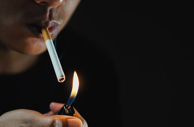 Close-up of hand holding cigarette lighter against black background