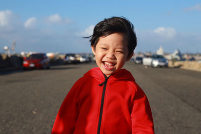 Portrait of boy smiling while standing on road against sky