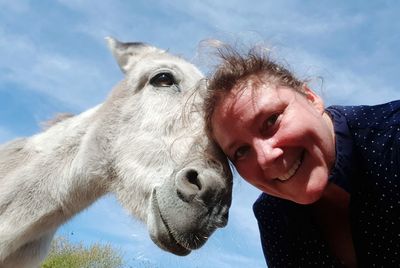 Portrait of smiling woman with donkey against sky