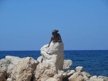 Rocks on cliff by sea against clear blue sky