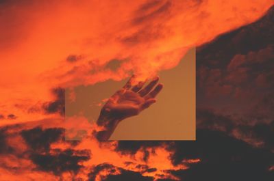 Low angle view of hand against dramatic sky during sunset