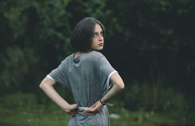 Young woman looking away while standing against trees