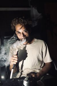 Portrait of young man smoking hookah at home