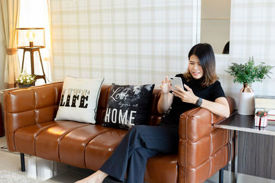 Young woman using phone while sitting on sofa