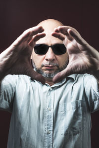 Portrait of a bearded and bald man wearing eyeglasses against a red dark background.