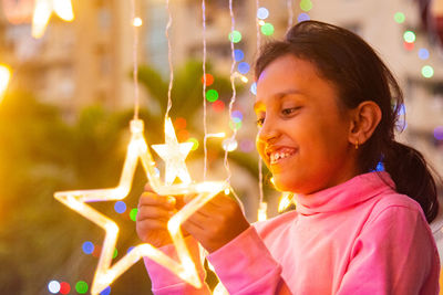 Side view of woman holding illuminated string lights