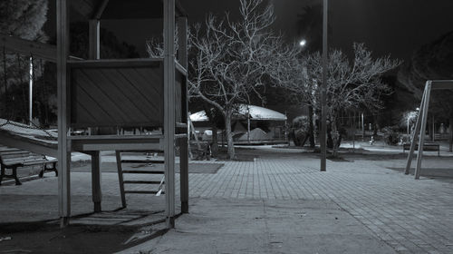 Empty chairs and tables by illuminated building at night