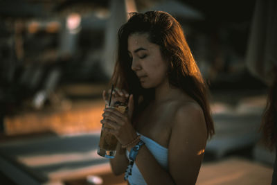 Young woman standing with drink during sunset
