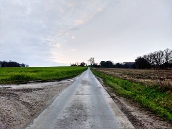 Surface level of road amidst field against sky