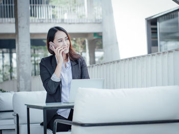 Smiling businesswoman talking on mobile phone while sitting by laptop at office