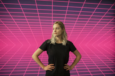 Portrait of young woman standing against pink wall