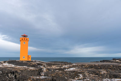 Lighthouse amidst sea and buildings against sky