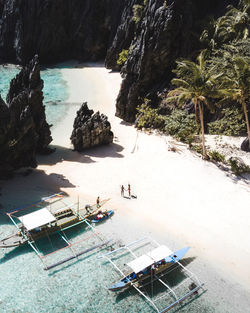 Aerial view of coast with white sand and tourists near sailboats on island with big rocks in elnido, philippines