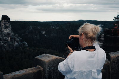 Rear view of woman photographing landscape against sky