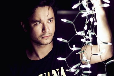 Close-up of young man holding illuminated string lights in darkroom