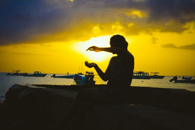 Silhouette woman gesturing while sitting pier against lake during sunset