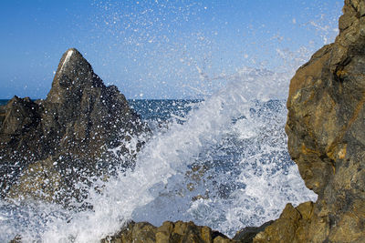 Sea waves splashing on rocks against sky