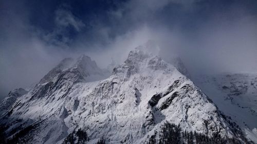 Low angle view of snowcapped mountain against sky in foggy weather