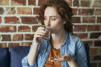 Young man drinking coffee while sitting against brick wall