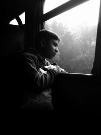 Side view of boy looking through window at home