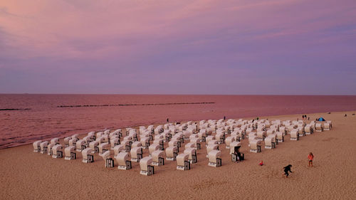 High angle view of hooded beach chairs at sea shore against sky during sunset