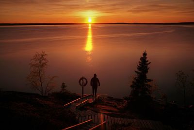 Silhouette person standing by tree against orange sky