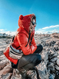 Midsection of woman sitting on rock against sky