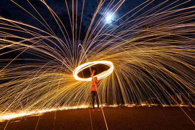 Woman spinning wire wool while standing on land at night