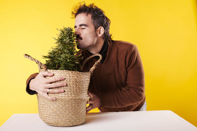 Side view of young man using mobile phone while sitting against yellow background
