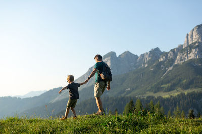Rear view of man walking on mountain against clear sky
