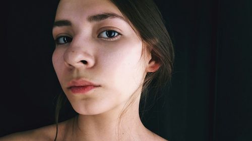 Close-up portrait of young woman against black background