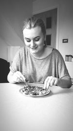 Smiling teenage girl having food while sitting on table at home