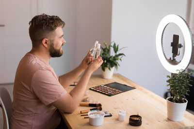 Side view of man using mobile phone while sitting on table