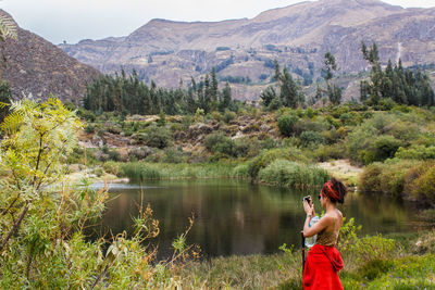 Woman photographing lake against mountains