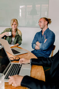 Male and female coworkers looking at laptop while brainstorming in office