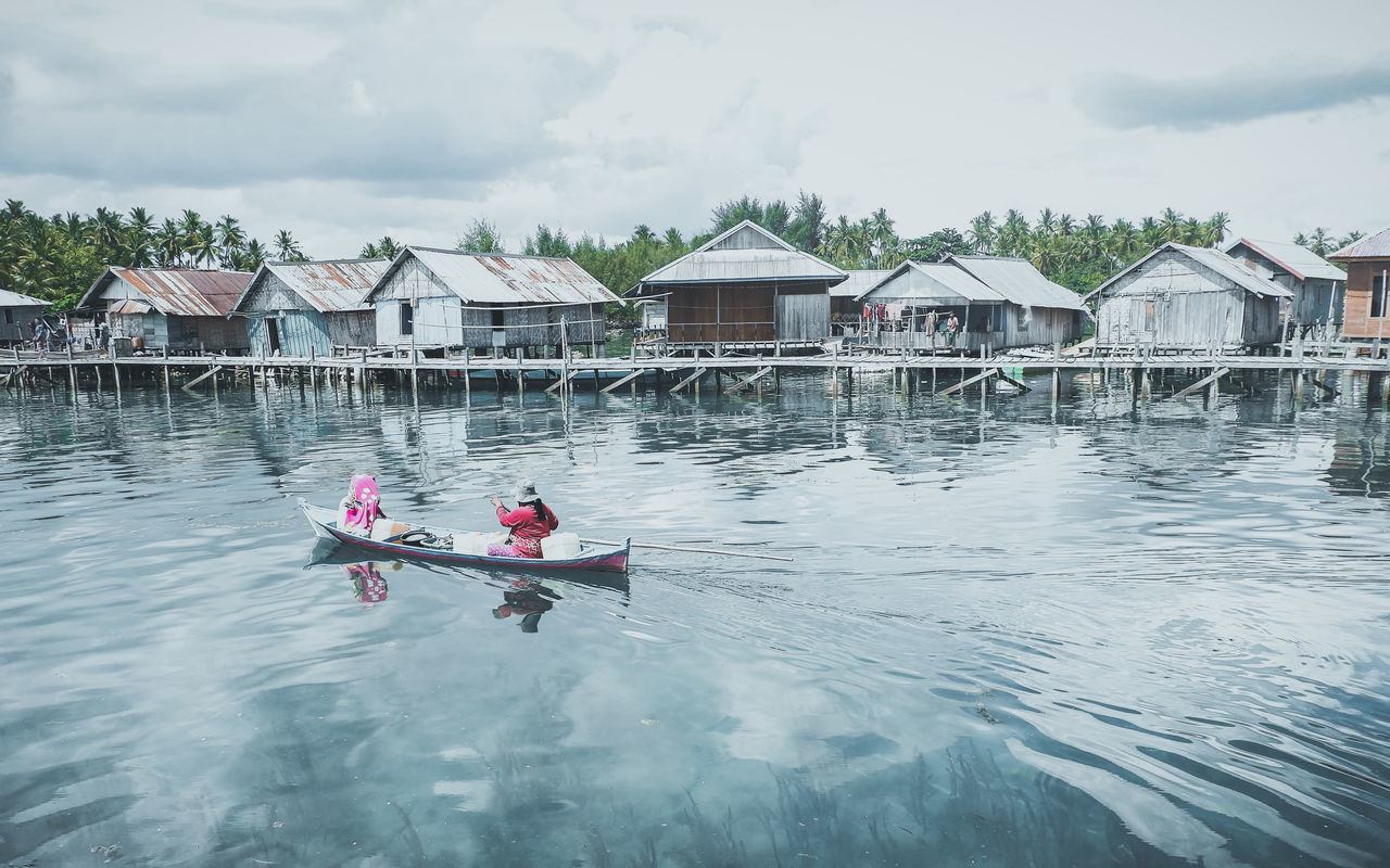 water, boating, architecture, nautical vessel, nature, transportation, built structure, building exterior, day, cloud, boat, house, men, vehicle, sky, adult, sea, building, rowing, oar, stilt house, mode of transportation, outdoors, group of people, lifestyles, paddle, sports, leisure activity, women, reflection, togetherness, watercraft, waterfront, travel, trip, vacation, kayak, residential district