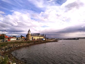 View of buildings by sea against cloudy sky