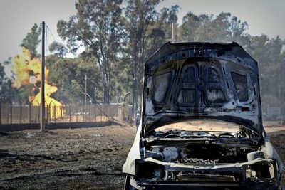 Damaged and burned car with open hood on dirt road