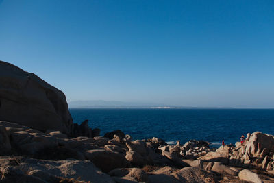 Rocks by sea against clear blue sky