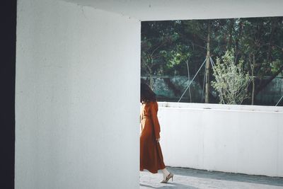 Woman standing by window against wall