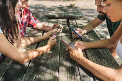 Midsection of friends using mobile phone on wooden table