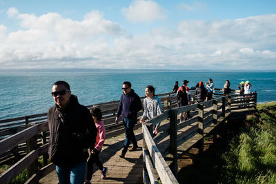 People standing on railing by sea against sky